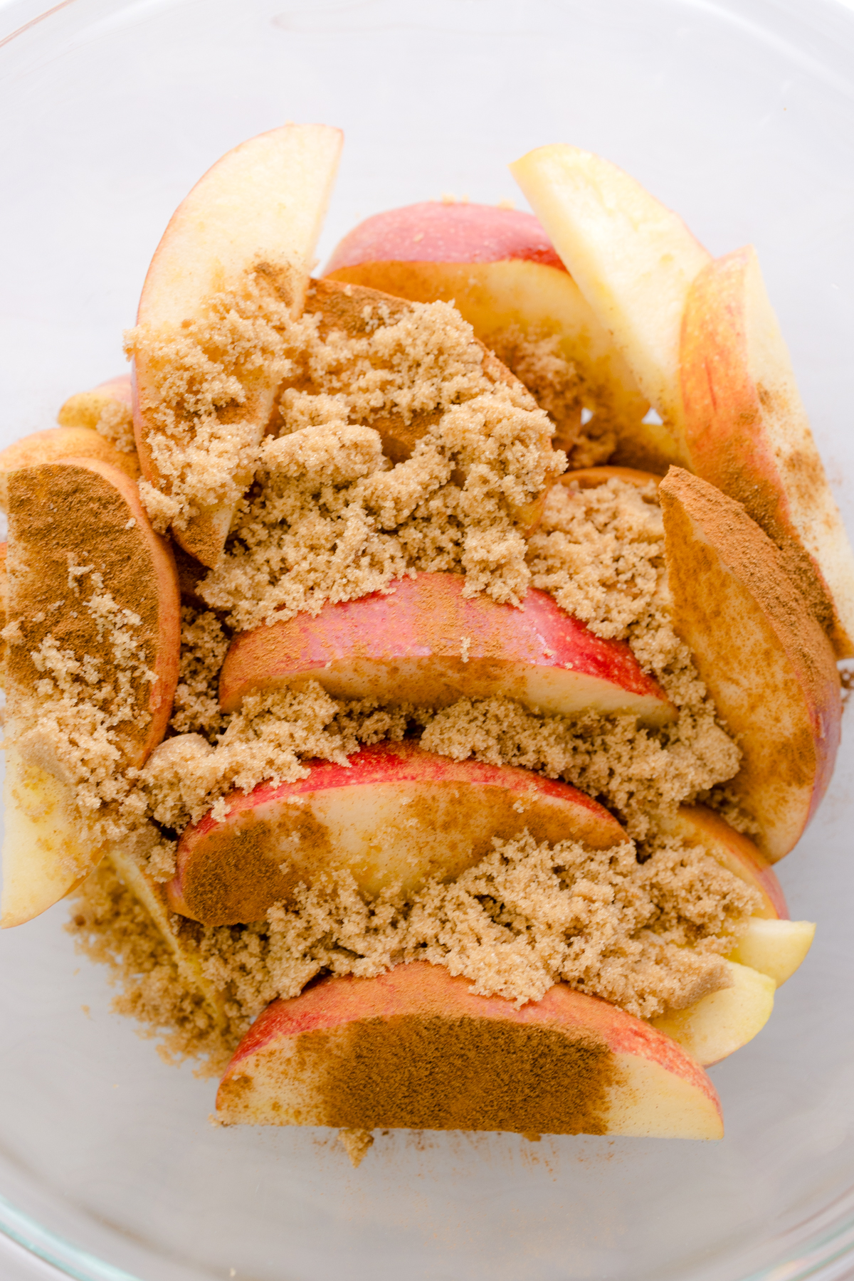 Overhead close up view of apples combined with cinnamon sugar mix in a glass dish.