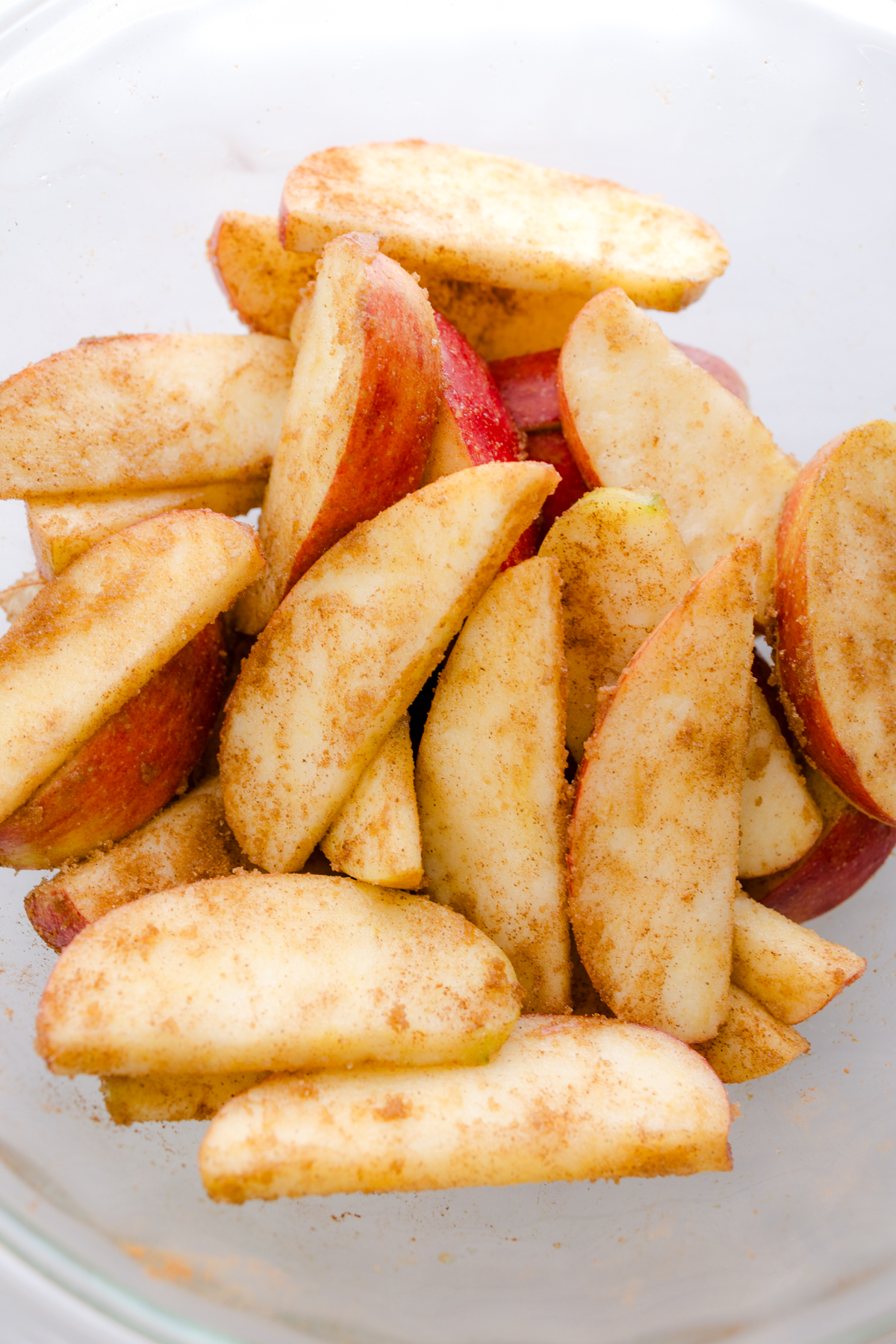 Overhead close up view of apples tossed with cinnamon sugar mix in a glass dish.