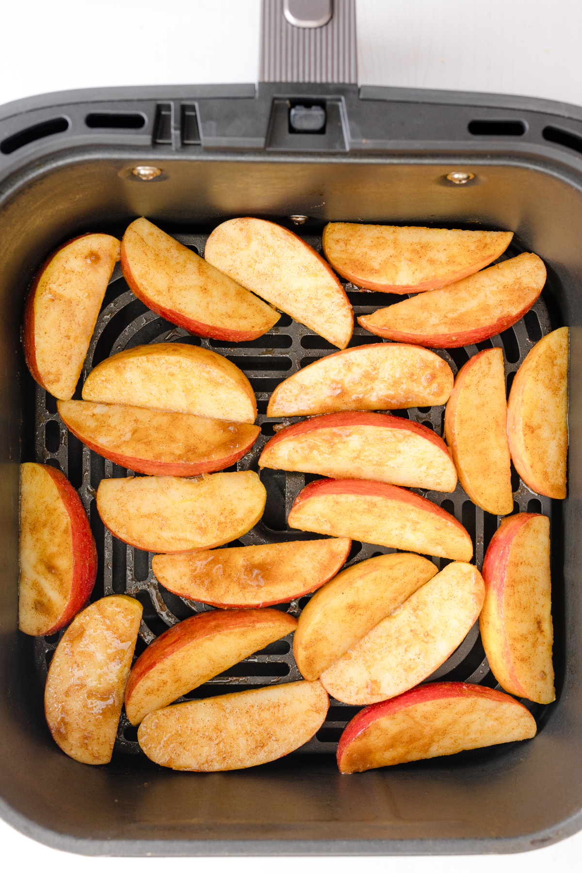 Overhead view of uncooked apples in an air fryer basket.