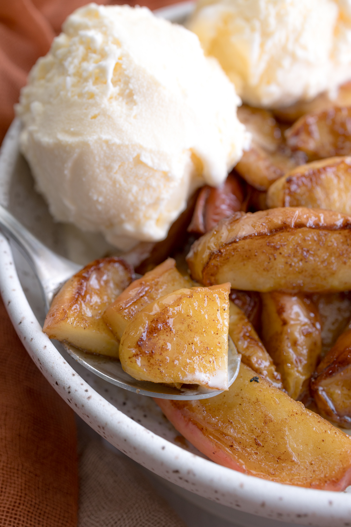 Angled close up view of Air Fryer Apples in a bowl with vanilla ice cream.