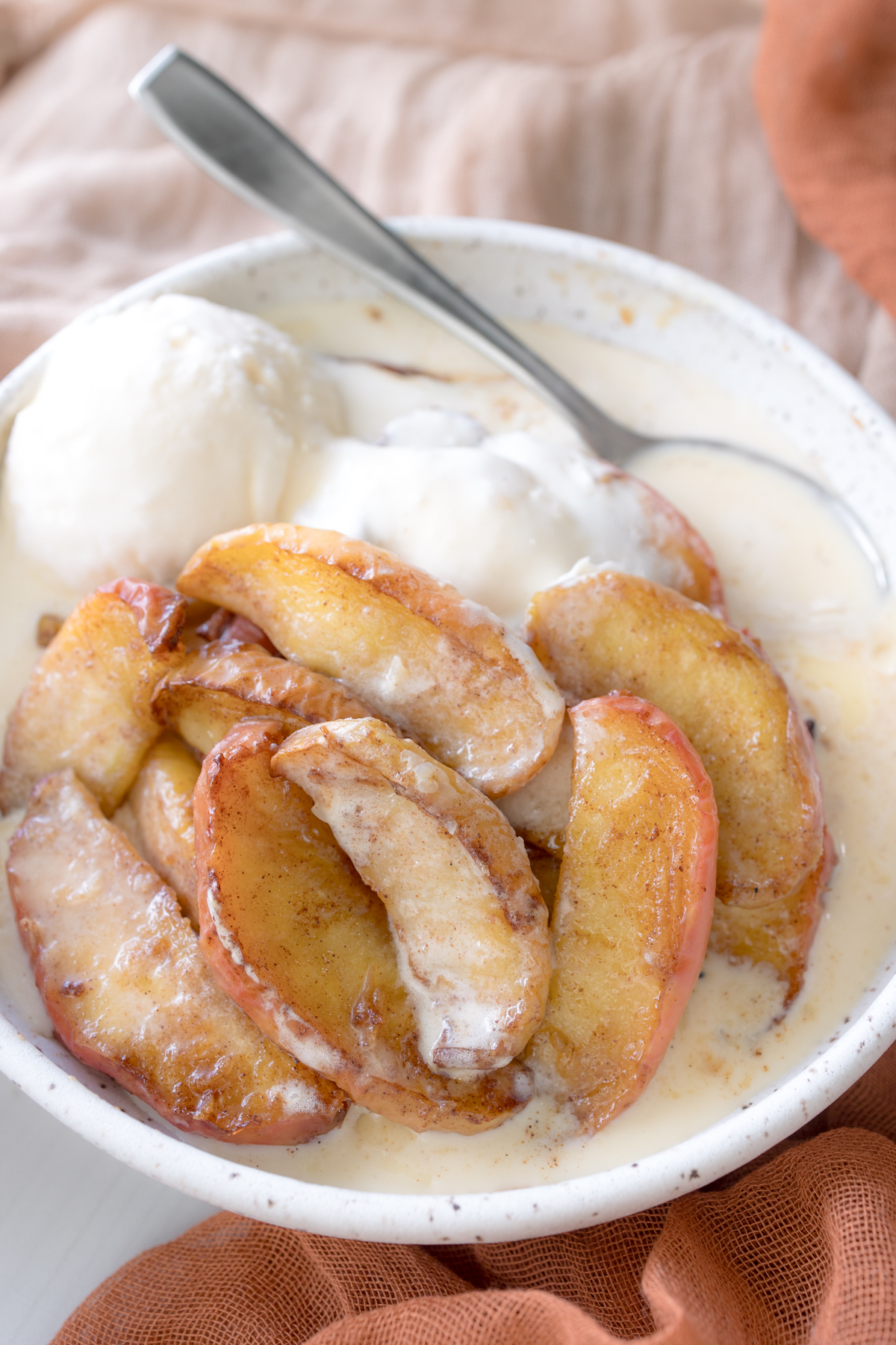 Angled view of Air Fryer Apples in a bowl with melted vanilla ice cream.