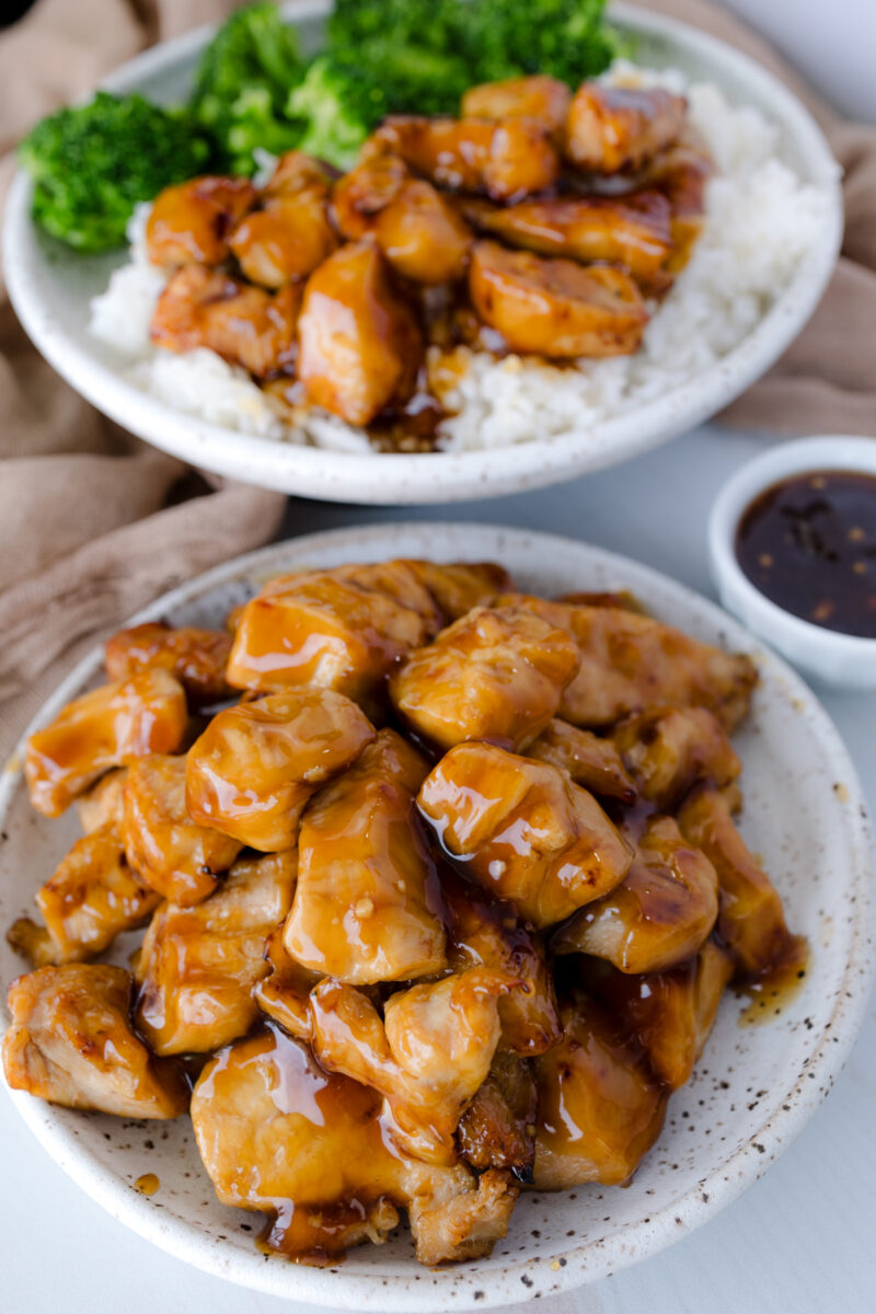 Overhead image of Air Fryer Teriyaki Chicken in a white bowl, next to a plate of Chicken Teriyaki served with broccoli and rice.