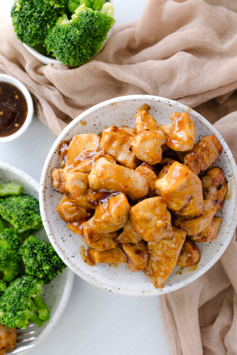 Overhead image of Air Fryer Teriyaki Chicken in a white bowl, next to a plate with broccoli.