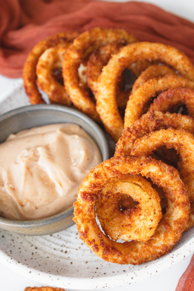 Angled view of a plate of Onion Rings with a dipping sauce.