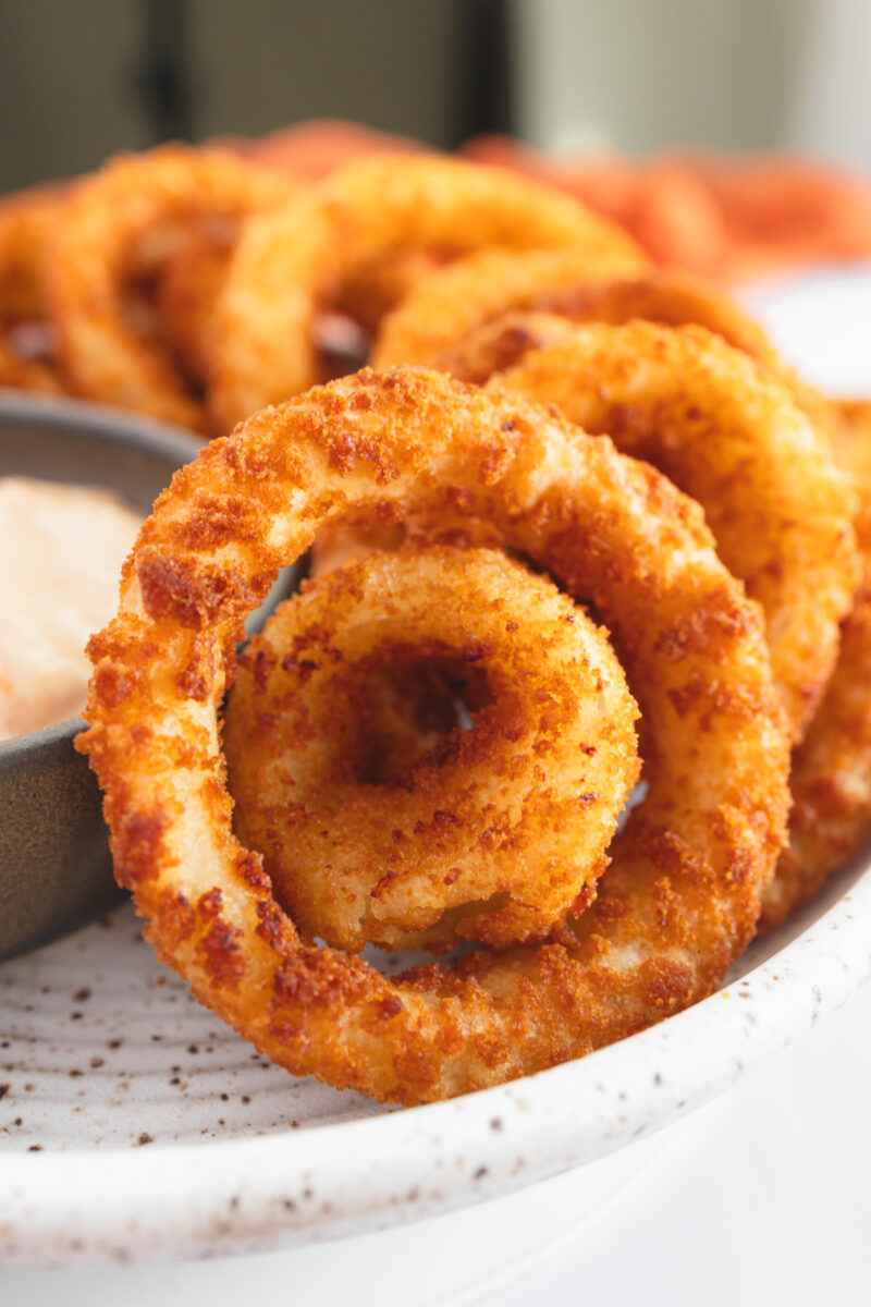 Close up view of a plate of Onion Rings with a dipping sauce.