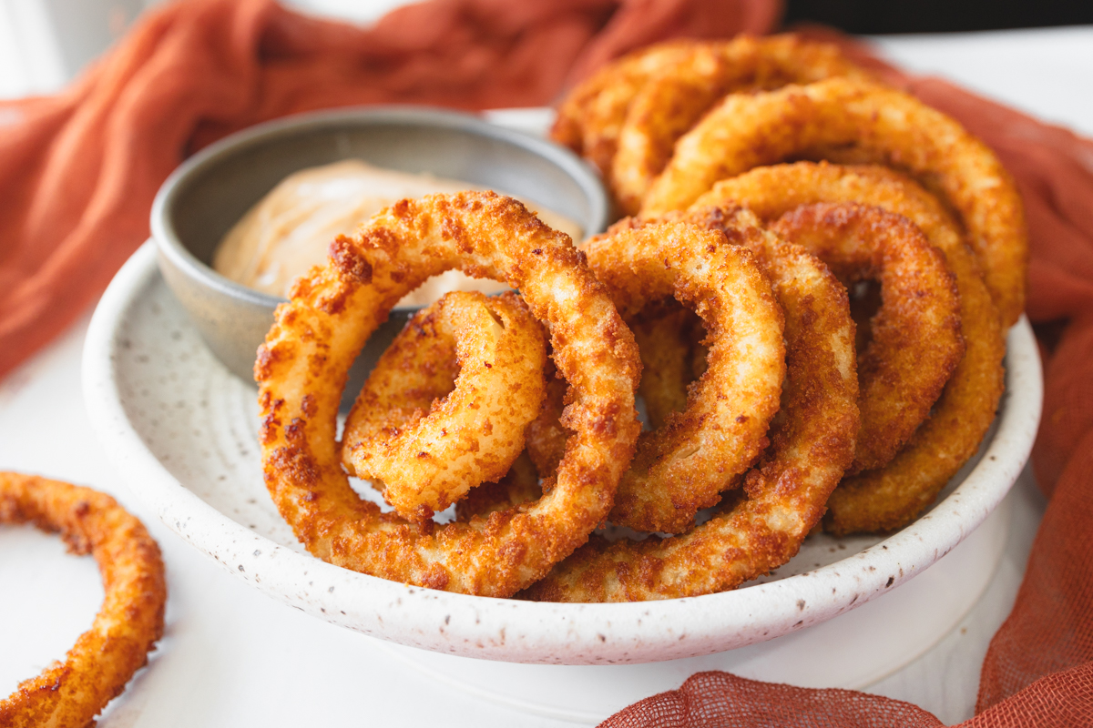 Angled view of a plate of Onion Rings with a dipping sauce.
