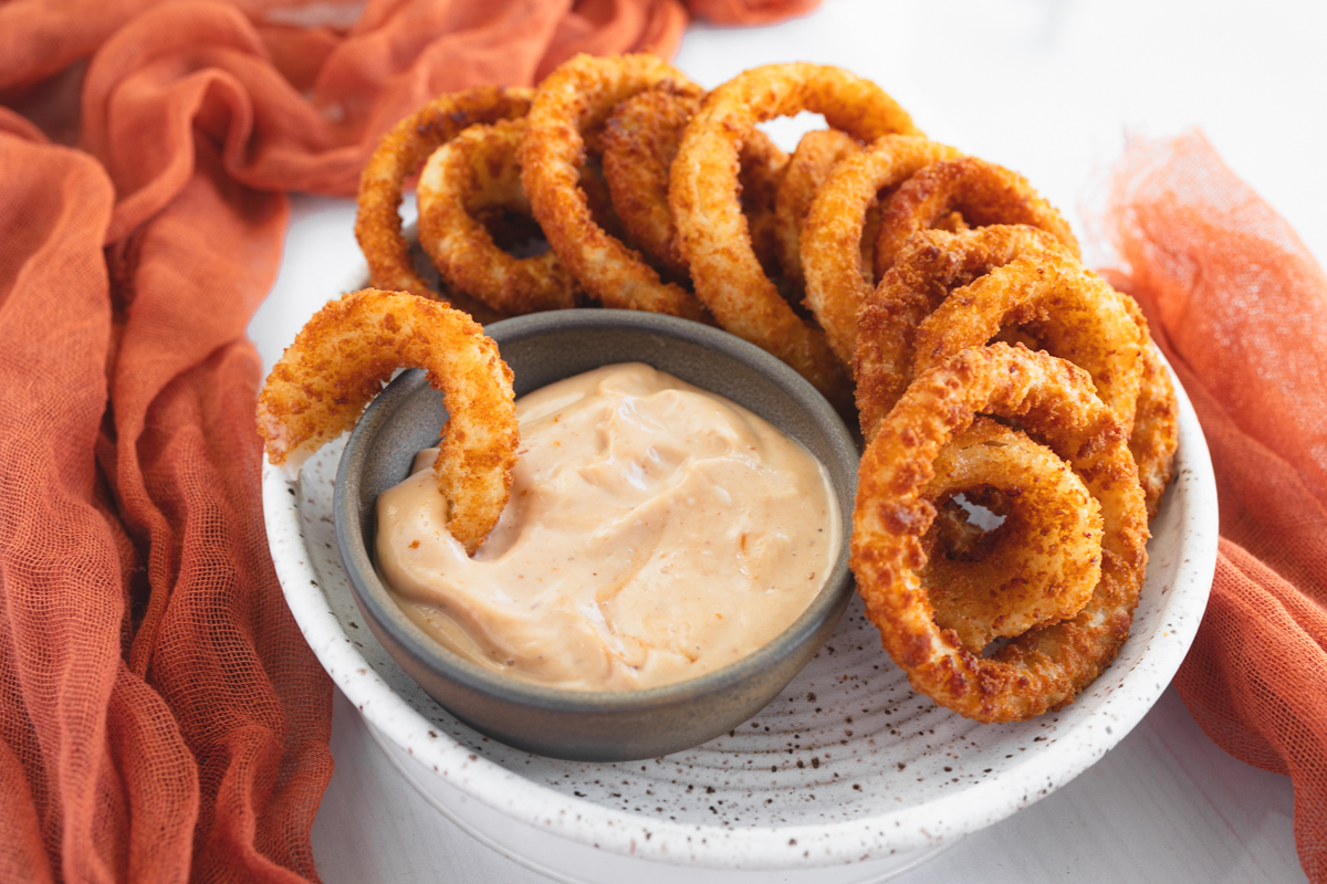 Angled view of a plate of Onion Rings with a dipping sauce.