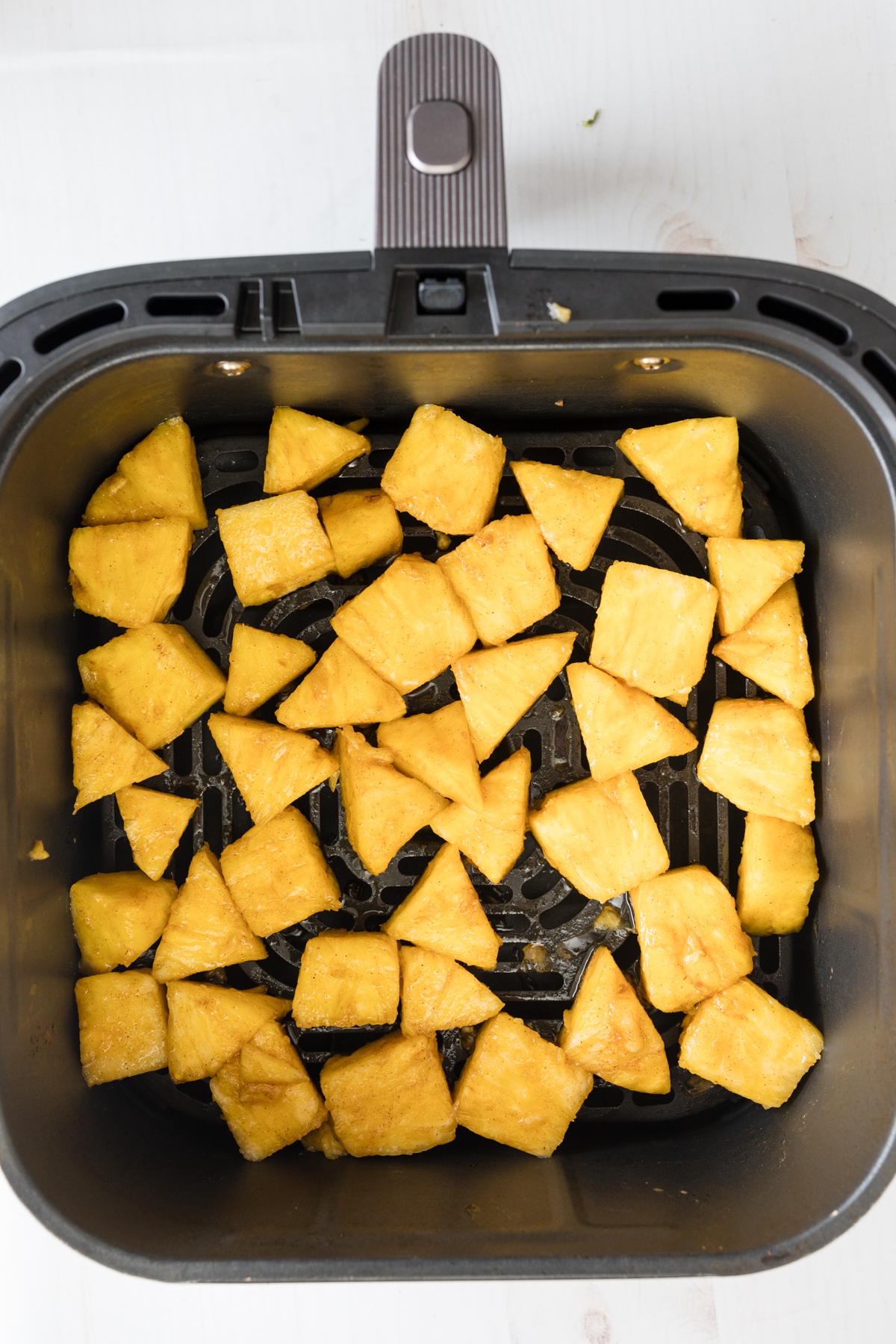 Overhead view of an air fryer basket with a single layer of pineapple chunks in it.