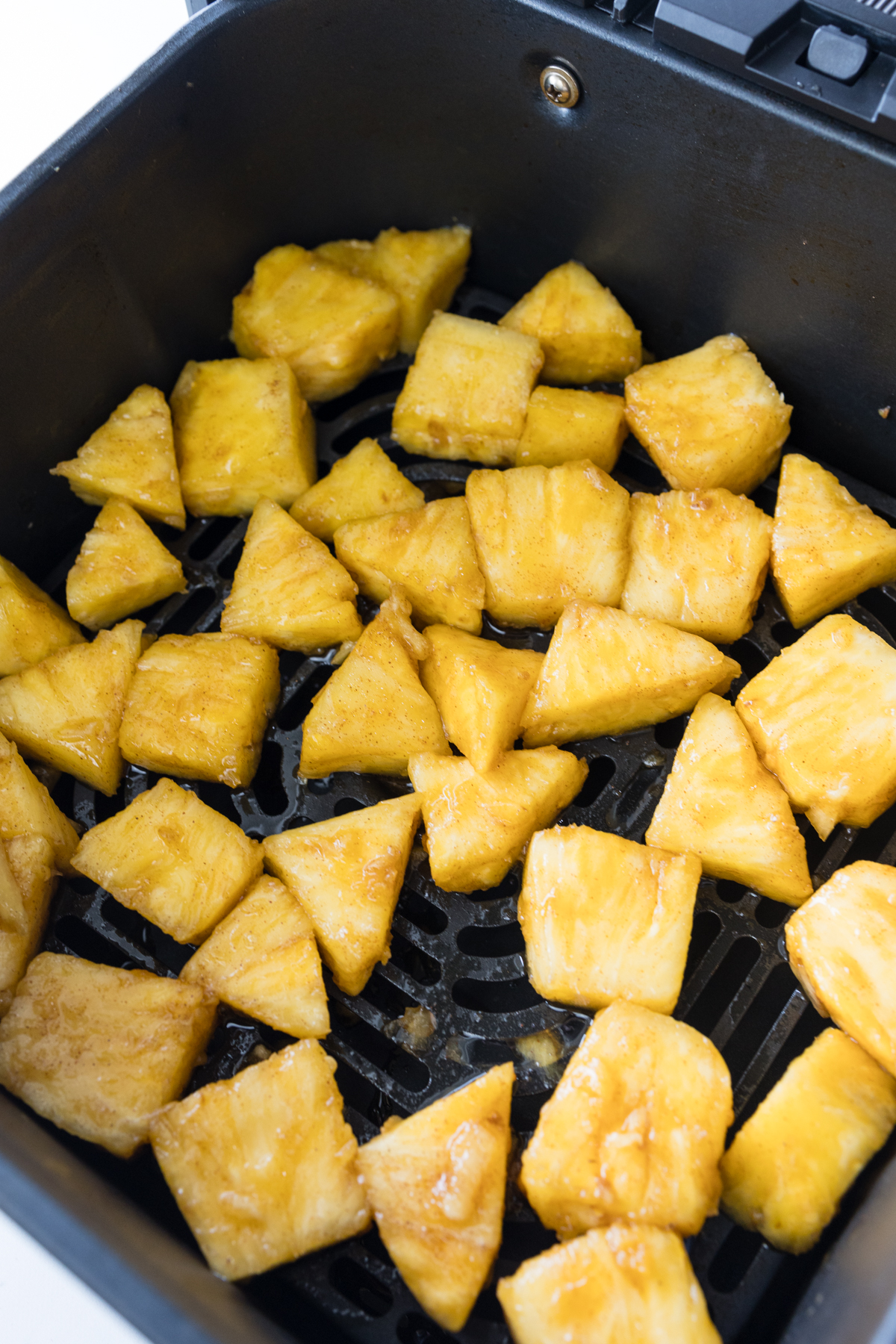 Angled view of pineapple chunks in an air fryer basket.