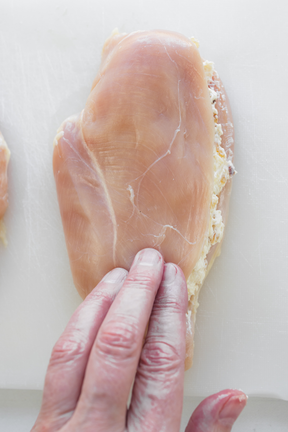 Close up overhead view of a sliced chicken breast that's been stuffed with filling, closed over and patted down flat.