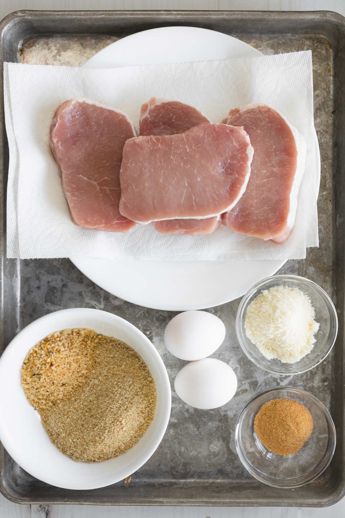 Top view of full ingredient setup with pork chops, bread crumbs, parmesan, and egg mixture.