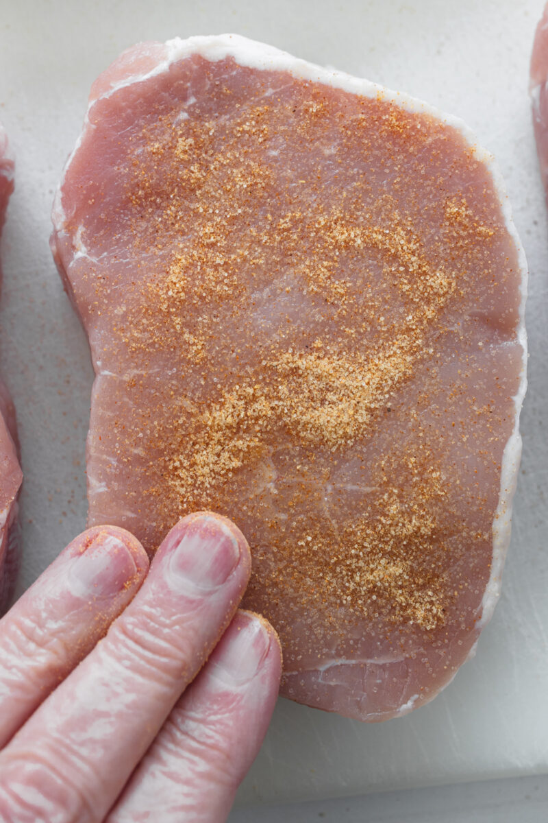 Sprinkling seasoned salt over a boneless pork chop for extra flavor.