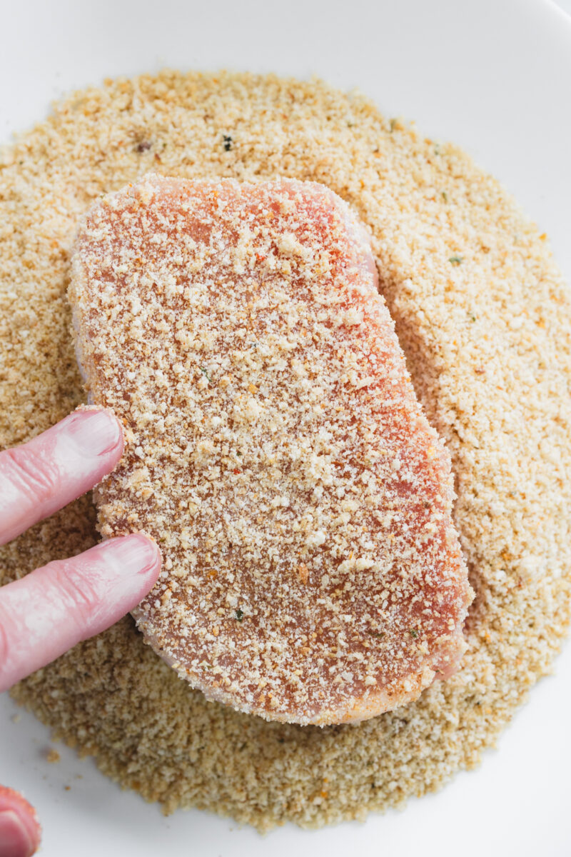 Pressing pork chop into bread crumb mixture for a crispy exterior.