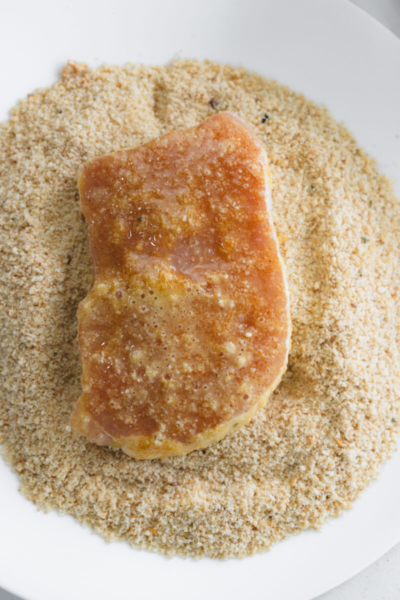 Dipping seasoned pork chop into bread crumbs for a crispy coating.