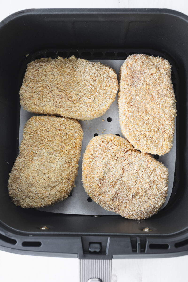 Breaded pork chops placed in air fryer basket ready for hot air cooking.