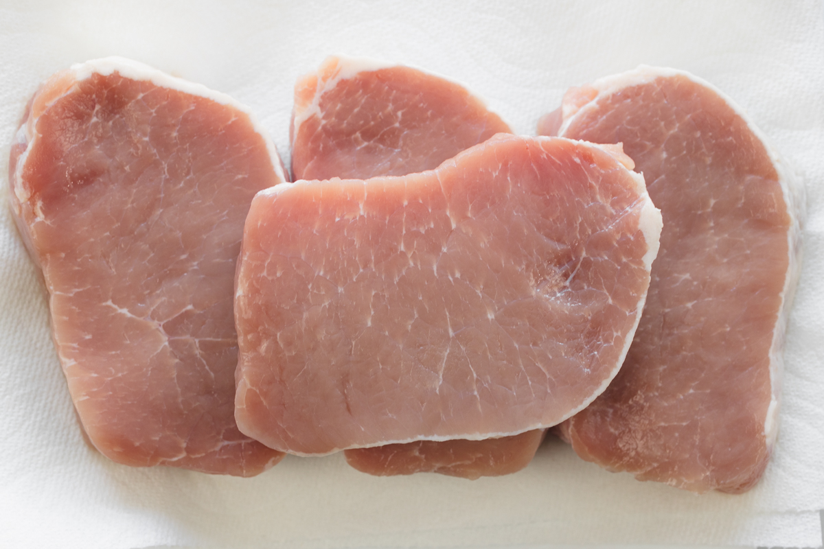Raw boneless pork chops ready for seasoning and breading.