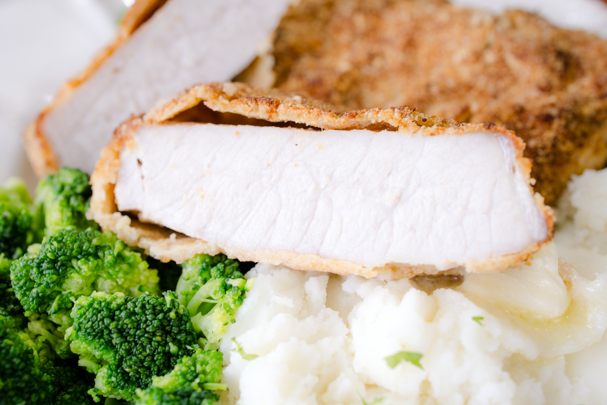 Close up of breaded pork chops served with mashed potatoes and green beans.