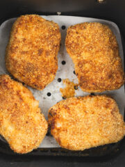 Crispy breaded pork chops in air fryer basket after cooking to juicy perfection.