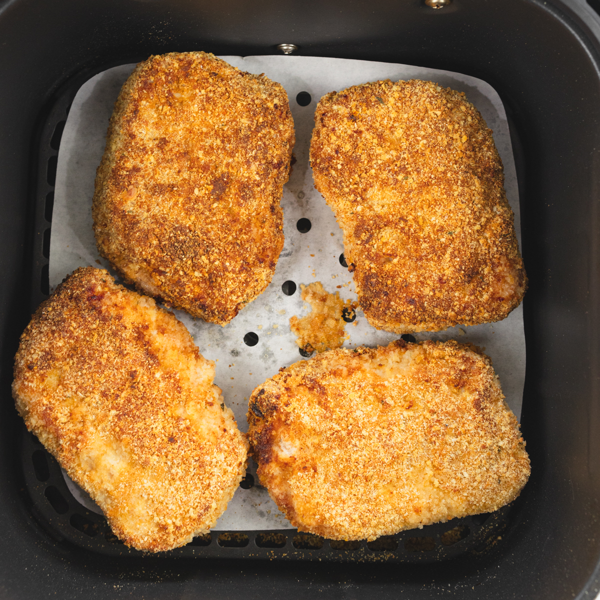 Crispy breaded pork chops in air fryer basket after cooking to juicy perfection.