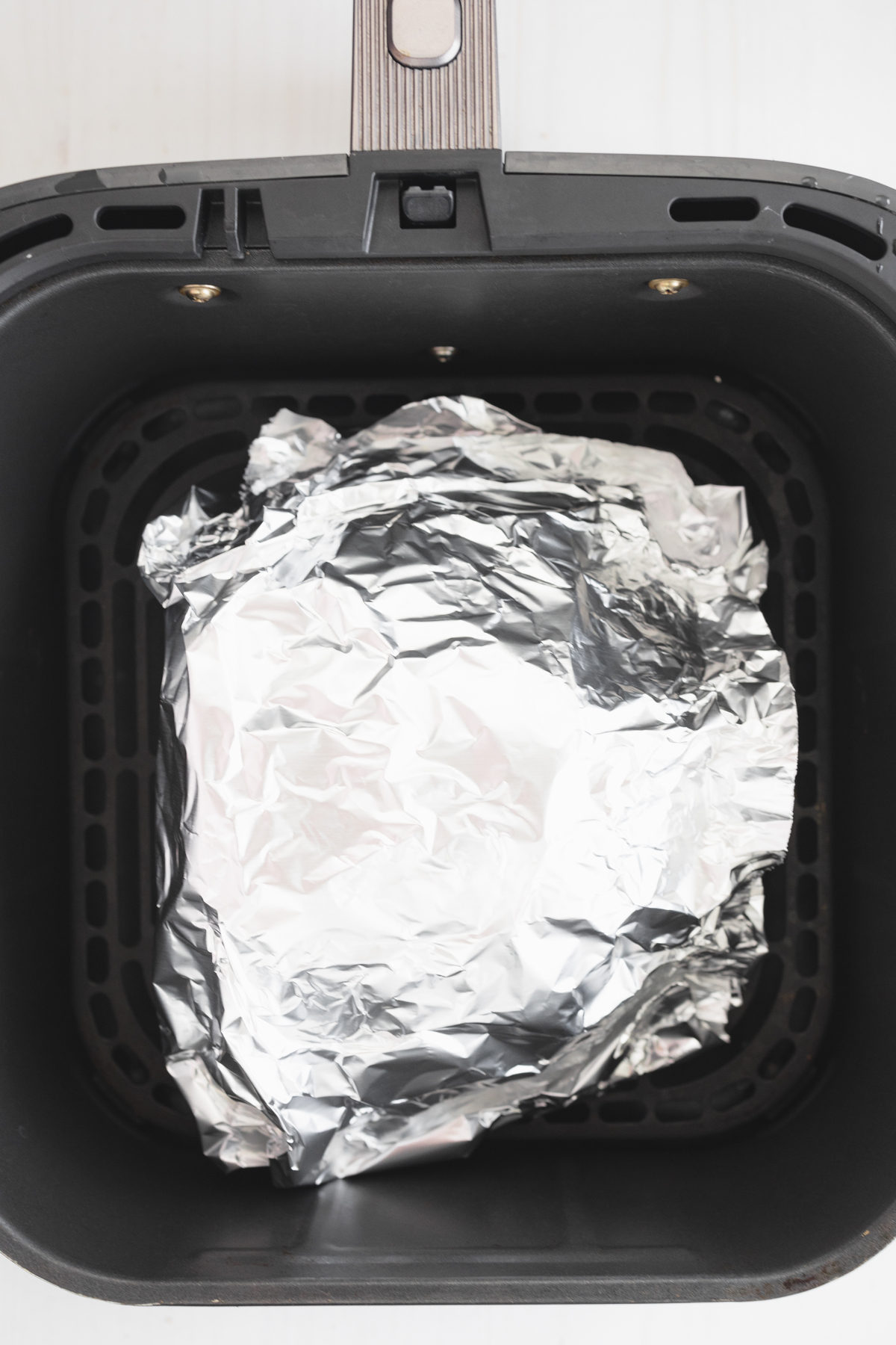 Overhead of a ham wrapped in tinfoil in an air fryer basket.