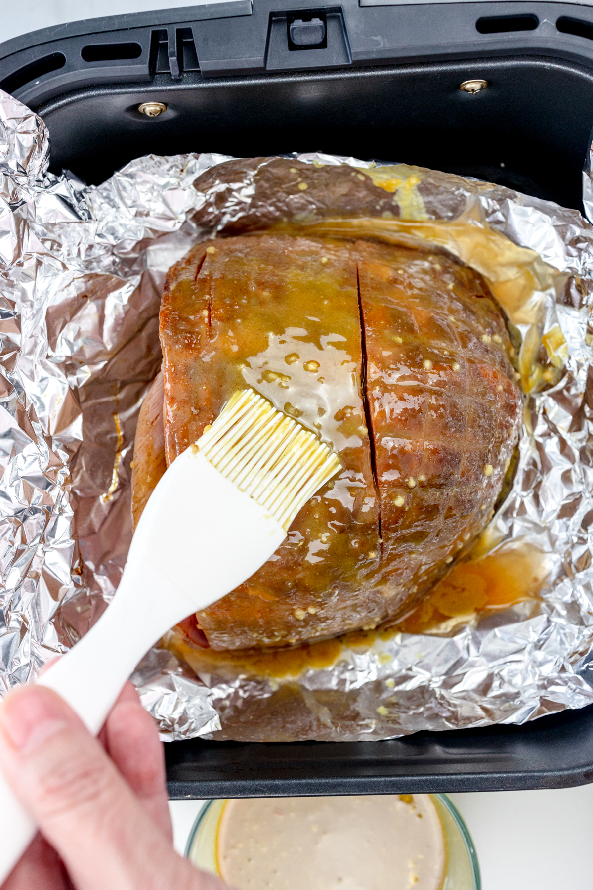 Overhead view of Air Fryer Ham being basted inside tinfoil in an air fryer basket.