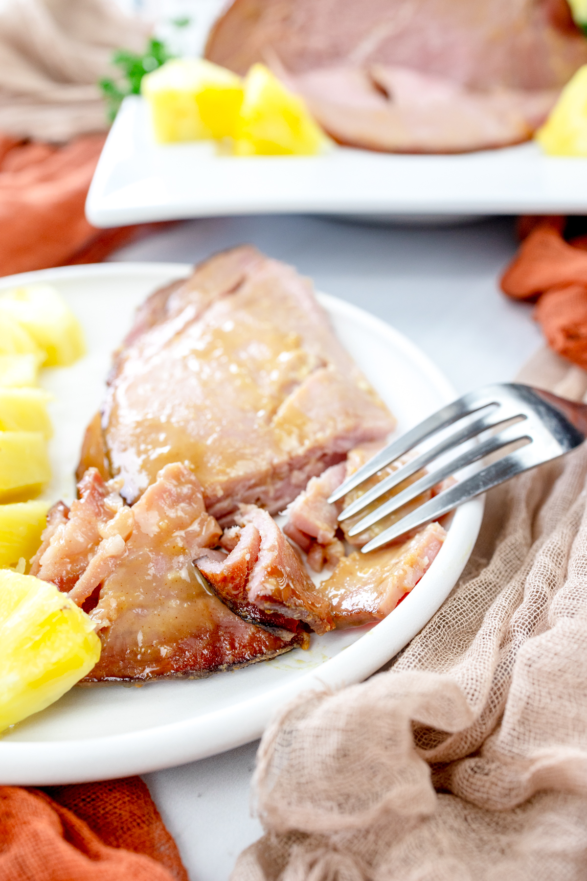 Angled view of Air Fryer Ham slices on a white plate with pineapple chunks.