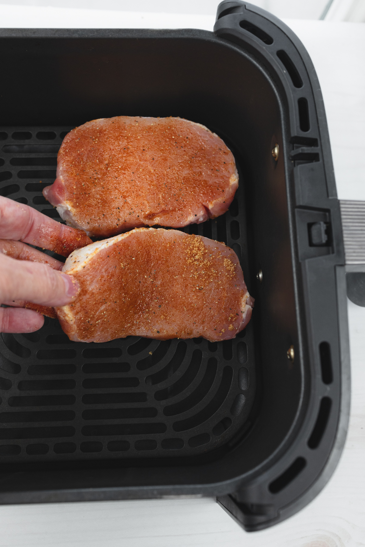 Close-up overhead view of two raw seasoned pork chops placed inside the air fryer basket, ready to cook.