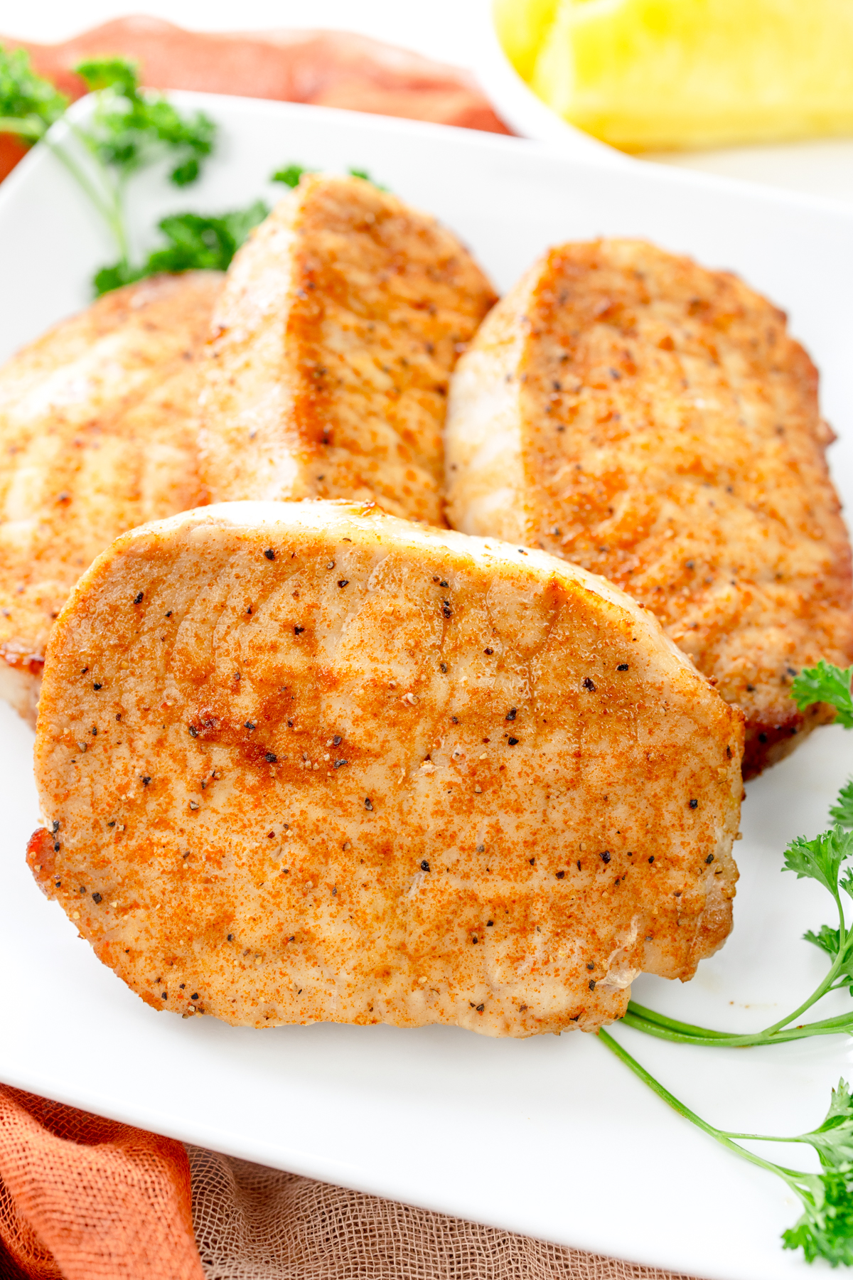 Close-up angled overhead view of four cooked, golden-brown seasoned pork chops arranged on a white plate with fresh parsley garnish.