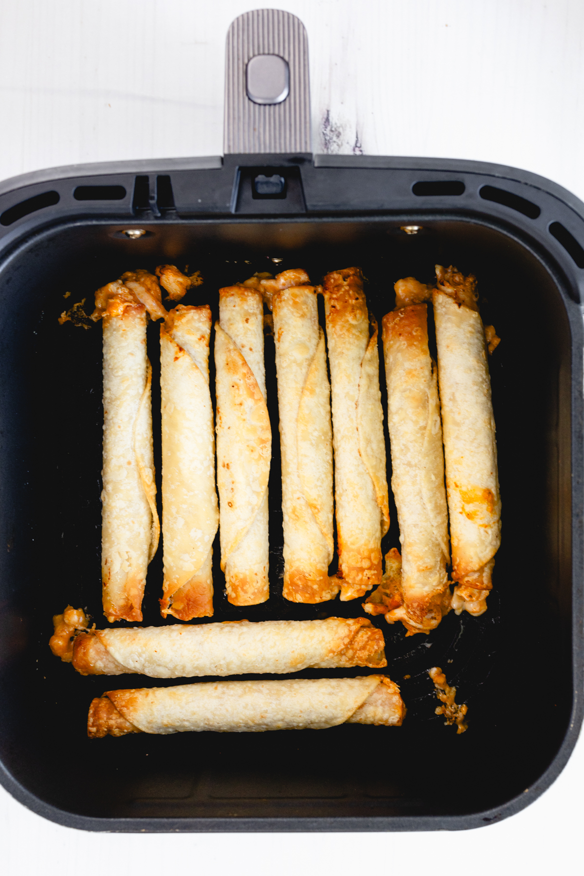 Overhead view of nine cooked chicken taquitos, golden and crisp, inside an air fryer basket.