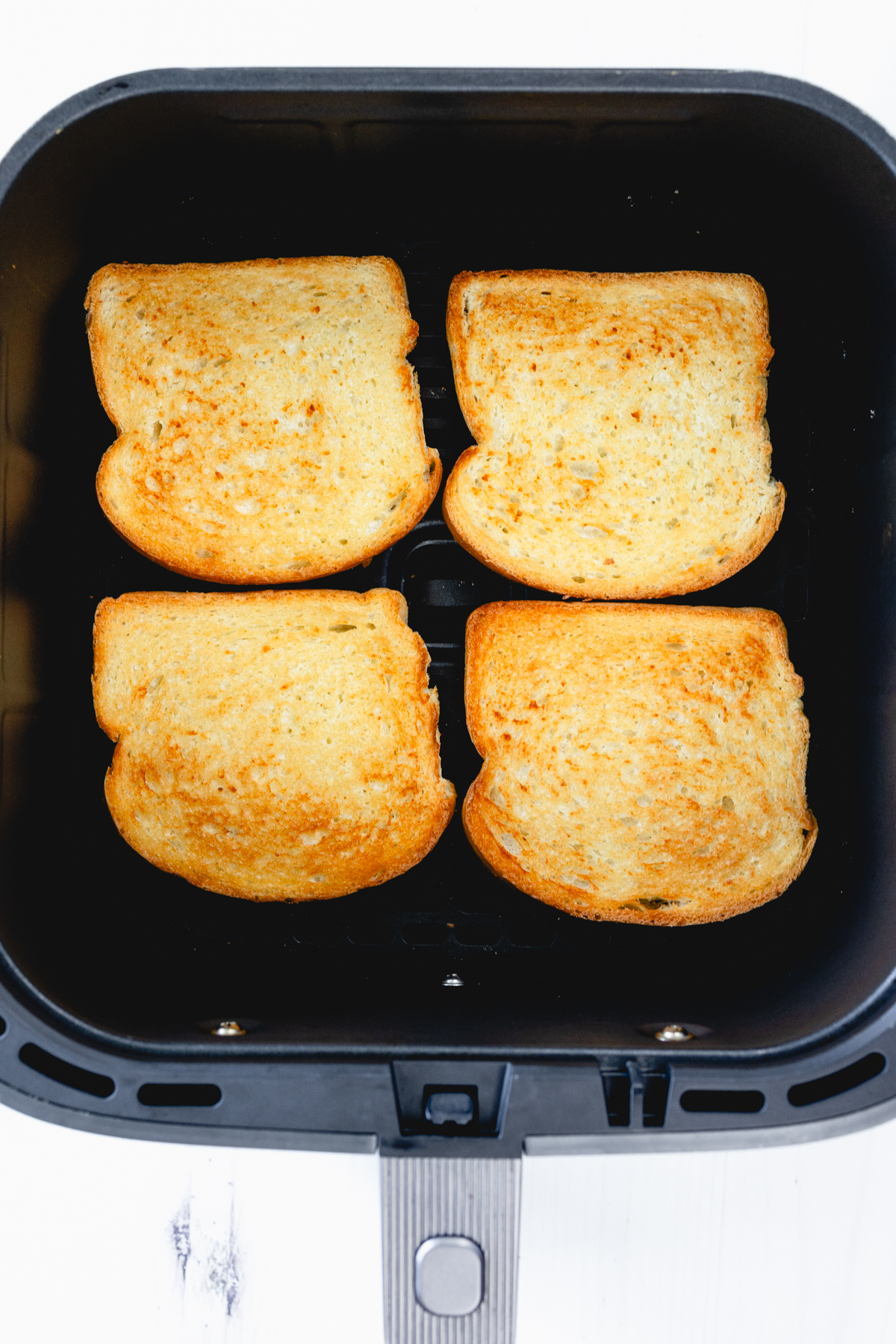 Overhead close-up of four slices of lightly toasted white bread in an air fryer basket.