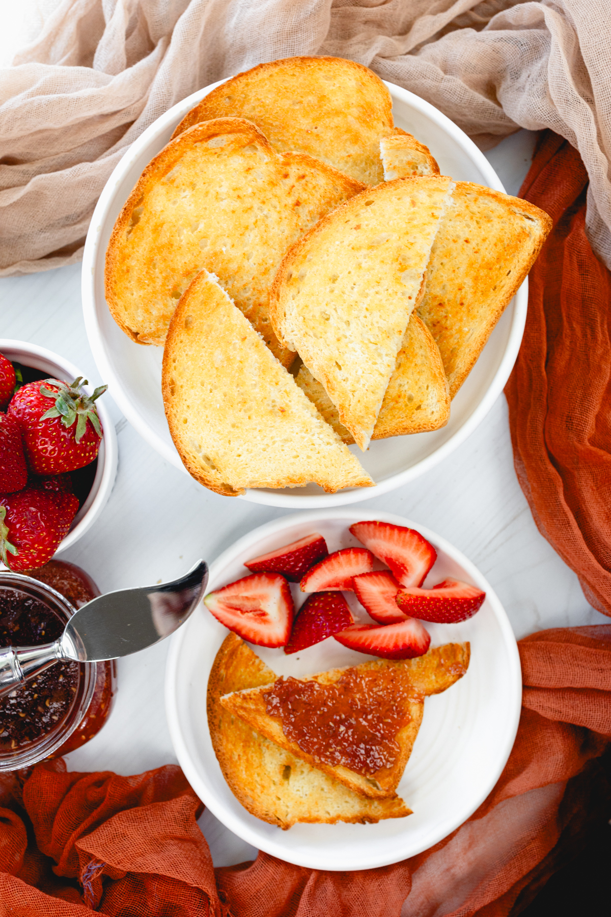 Angled close-up view of golden, crisp slices of toast served on a white plate with strawberries and jam nearby.