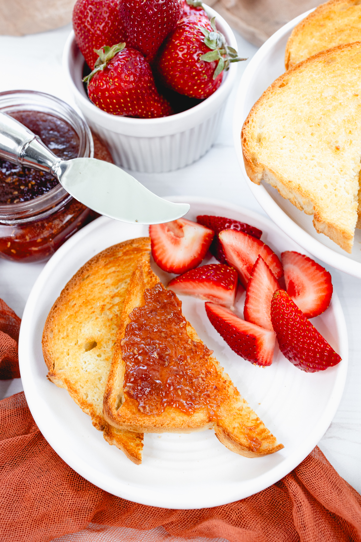 Close-up overhead view of golden-brown toasted bread on a white plate served with sliced fresh strawberries and jam.