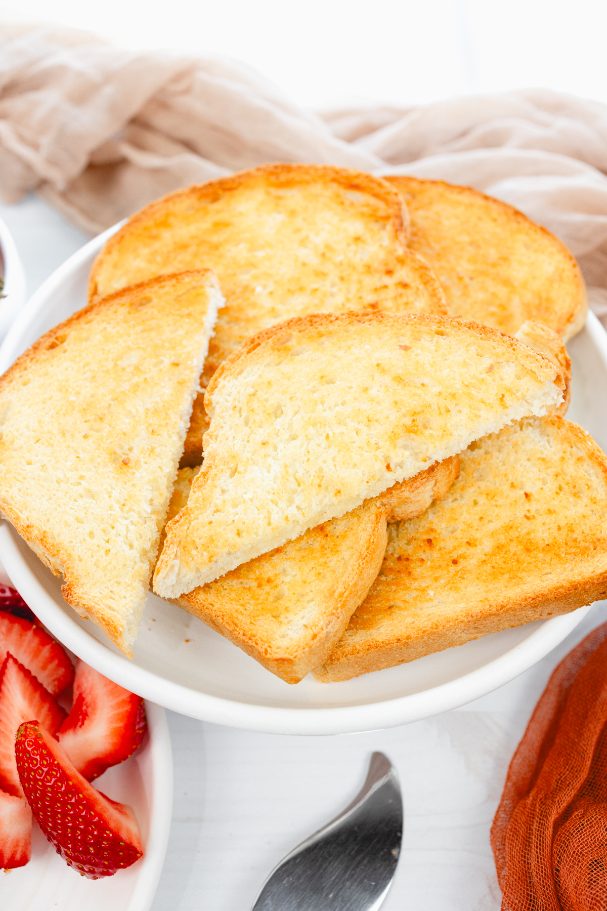 Close-up overhead angled view showing golden toast slices arranged on a white plate, alongside fresh strawberries and jam.